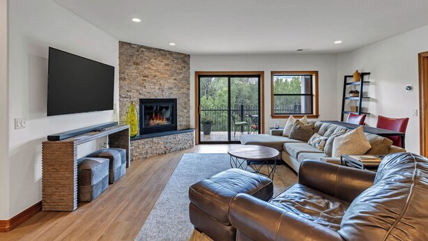 A modern living room with a fireplace, a flat-screen TV, leather sofas, and a dining area. - Riverfront Luxury- Minutes to Skiing+Garage+Walk to shops & restaurants! (Edwards)