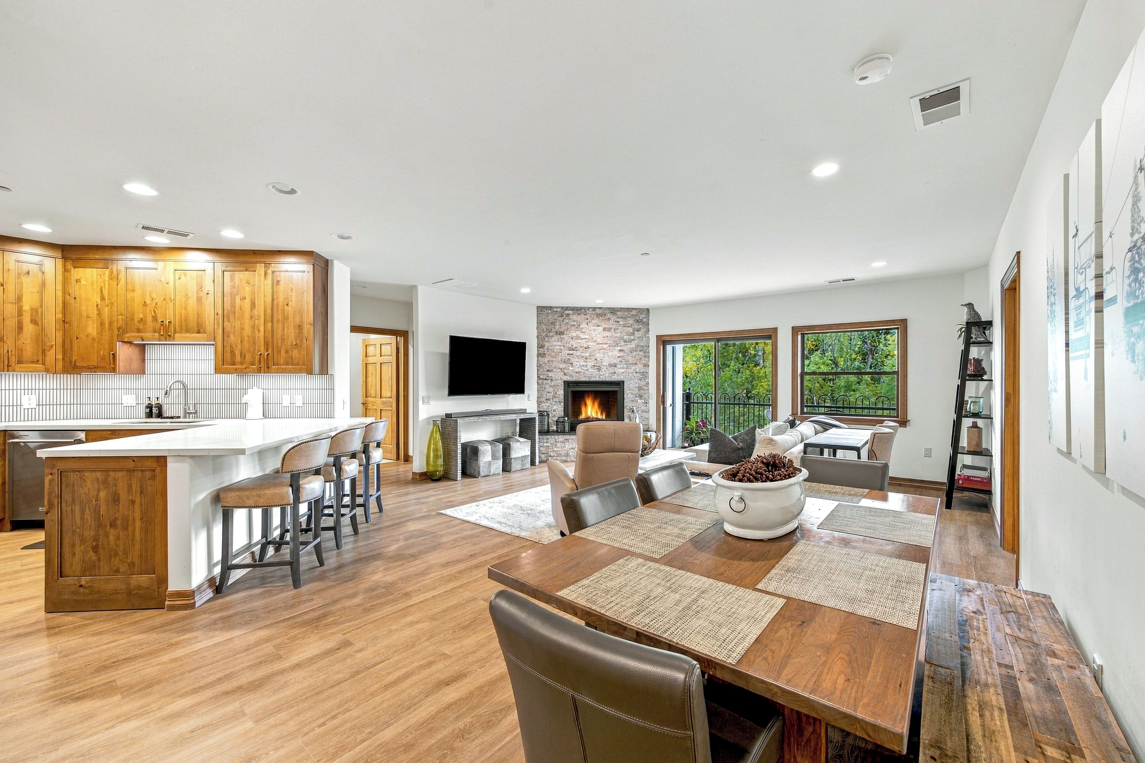 A modern kitchen with wooden cabinets, a central island with bar stools, a flat-screen TV, and a stone fireplace.