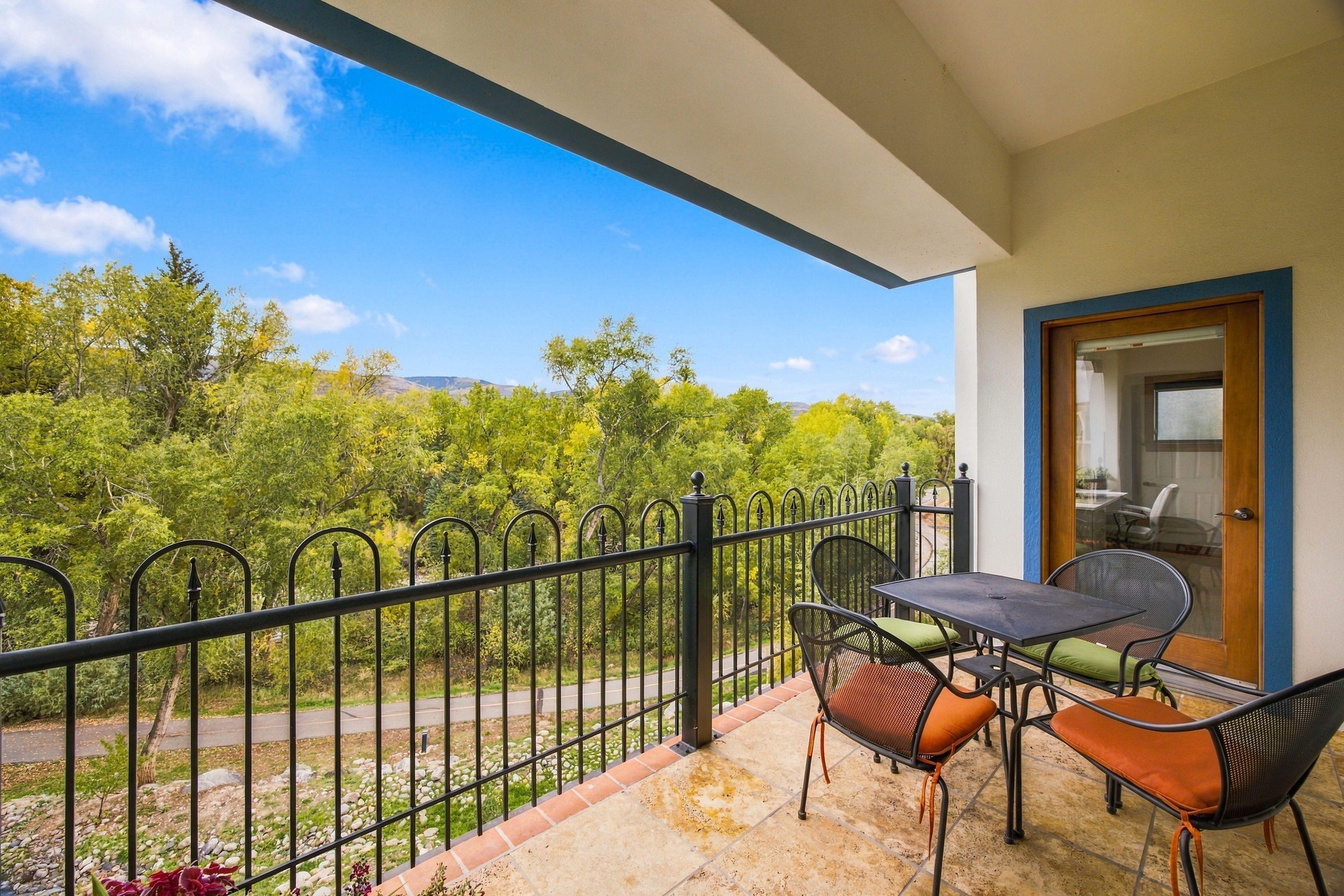 A balcony with a table and chairs, a door, and a view of a green landscape.