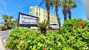 A sign for Symphony Beach Club with a building in the background.