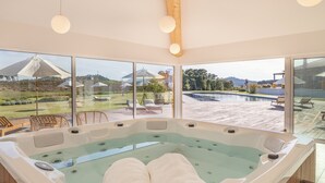 A spa area with a hot tub, large windows, and a view of a pool and garden. - Resort Rural Quinta do Carrascal (Rio Maior)