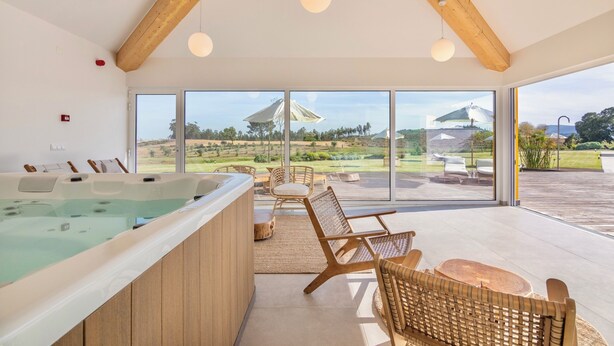 A modern spa area with a hot tub, wicker furniture, and large windows offering a view of the countryside. - Resort Rural Quinta do Carrascal (Rio Maior)