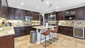 A modern kitchen with dark wood cabinets, granite countertops, stainless steel appliances, and a central island with bar stools. - Desert Oasis in Palm Springs/Indio, California (Indio)