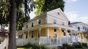 A two-story house with a porch, white railings, and a small garden area.