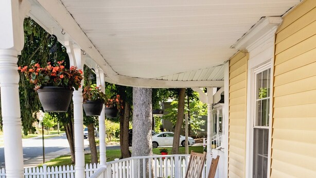 A covered porch with wooden chairs and hanging flower baskets.