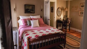 A bedroom with a wooden bed, a desk, and a chair. There is a door leading to another room.
