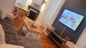 A modern living room with a wooden floor, a grey sofa, a TV, and a fireplace. - Cosy new apartment  (Vic-sur-Cère)