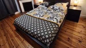 A bedroom with a wooden floor, a bed with patterned bedding, a fireplace, and a large floral artwork on the wall. - Cosy new apartment  (Vic-sur-Cère)