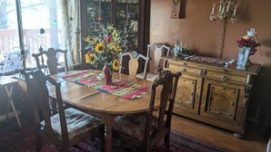 Een eetkamer met een houten tafel, stoelen, een vaas met zonnebloemen, een kroonluchter en een houten kast met lades.