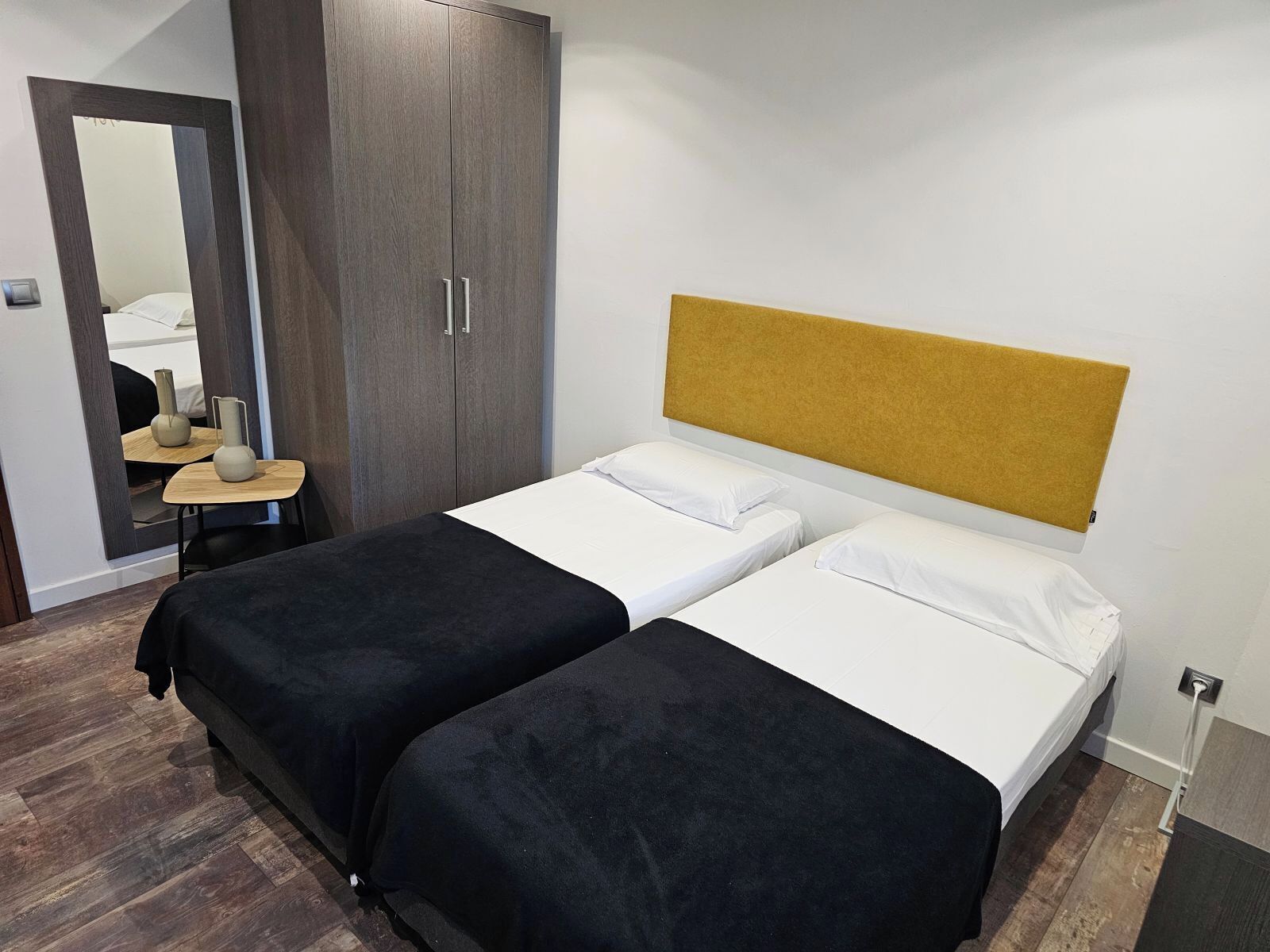 Una habitación de hotel con dos camas, un armario, un espejo y una pequeña mesa con jarrones.