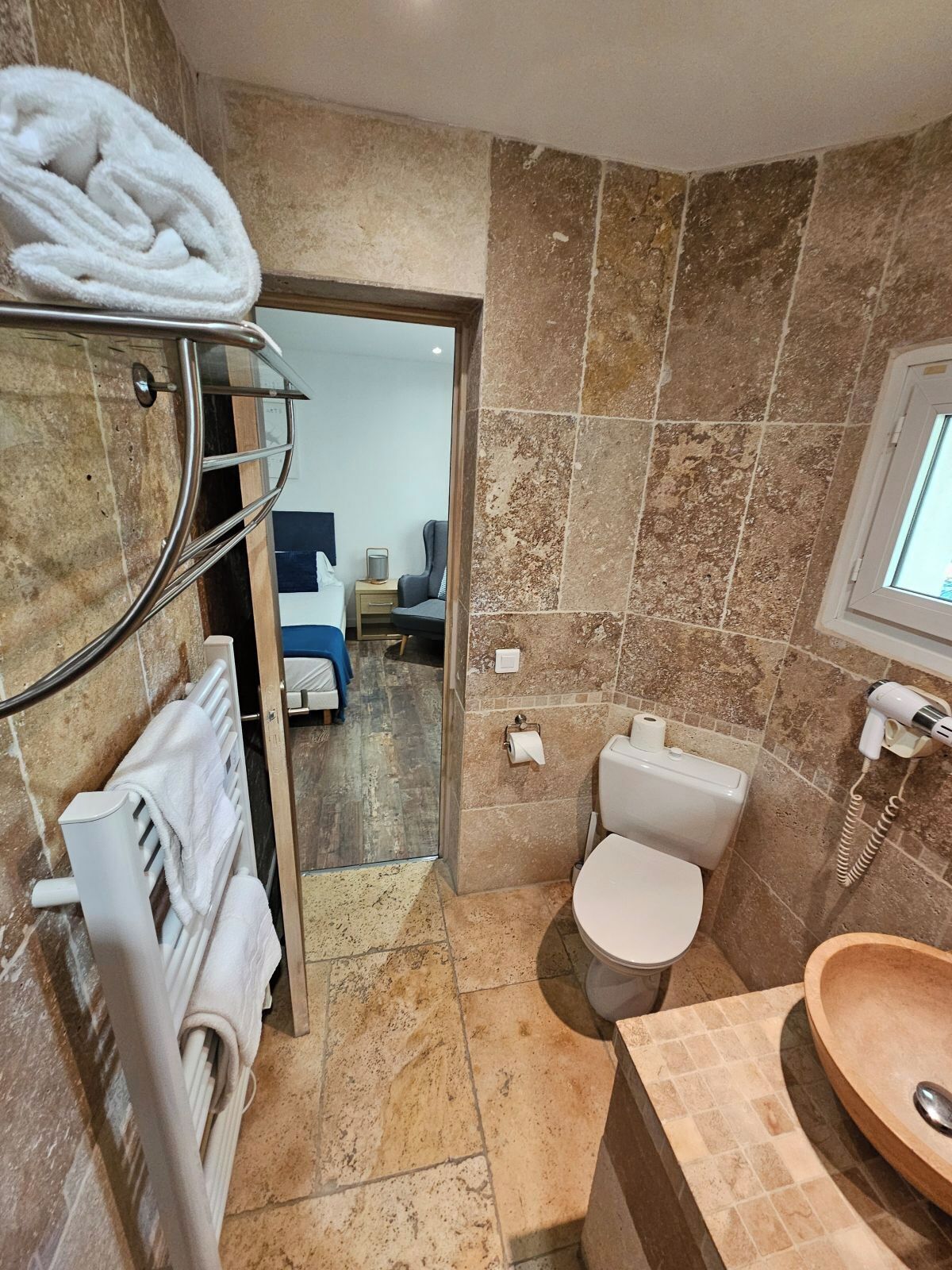 A bathroom with a shower, toilet, and sink. There is a towel rack with towels, a mirror, and a window.