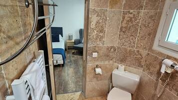 A bathroom with a shower, toilet, and sink. There is a towel rack with towels, a mirror, and a window.