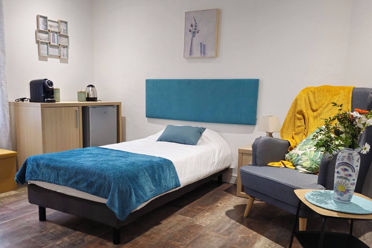 Un dormitorio moderno con una cama, un sofá, una cafetera y un florero con flores.