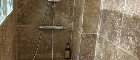 A shower with a handheld showerhead and a handheld faucet, a bottle of shampoo, and a window with frosted glass.