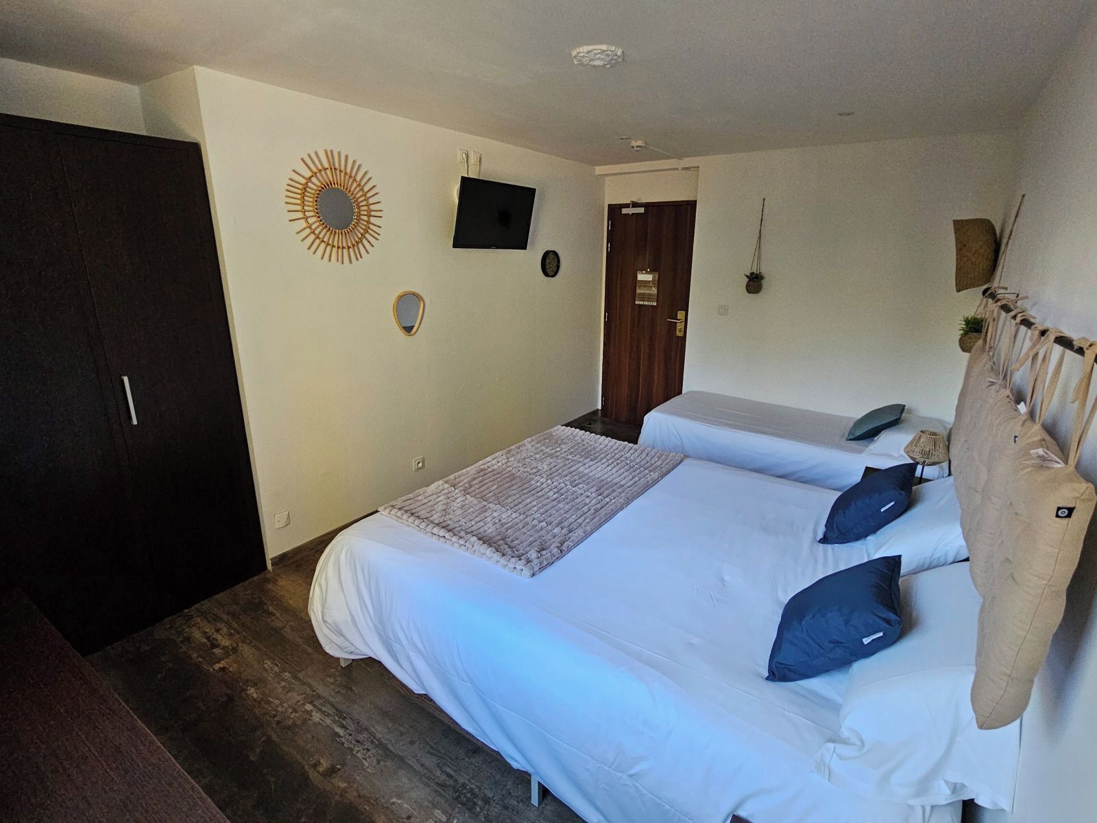 Un dormitori amb dos llits individuals, un armari fosc, un televisor a la paret i una porta que dona a una altra habitació.