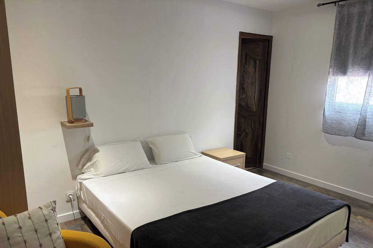 Un dormitorio ordenado con cama, mesita de noche y una pequeña estantería con espejo.