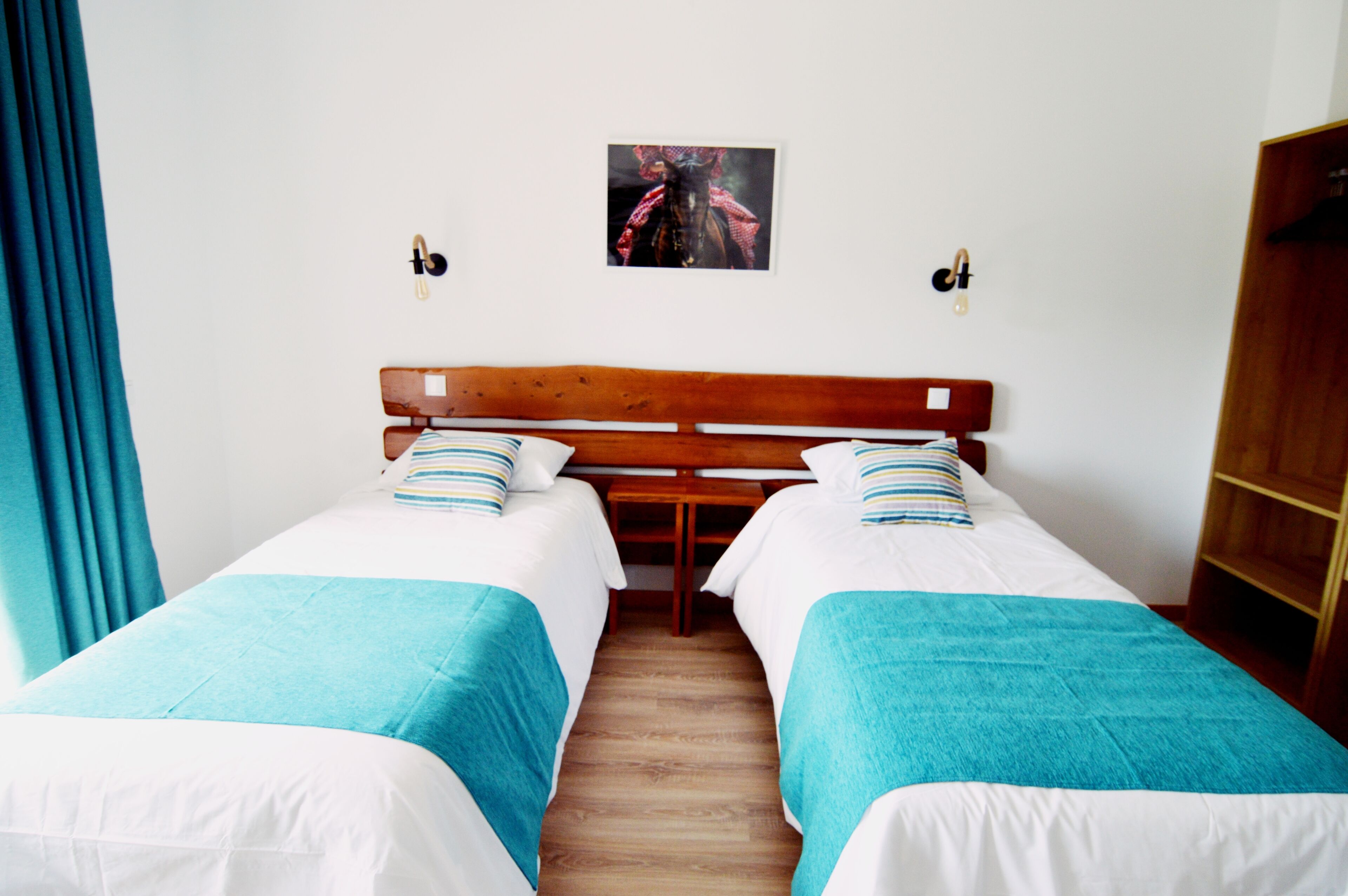 Una habitación con dos camas individuales, cada una con una colcha azul y blanca, cabecero de madera y un cuadro enmarcado en la pared.