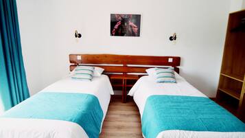 Una habitación con dos camas individuales, cada una con una colcha azul y blanca, cabecero de madera y un cuadro enmarcado en la pared.