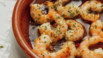 A terracotta dish with cooked shrimp garnished with herbs, served on a white plate with a textured pattern.