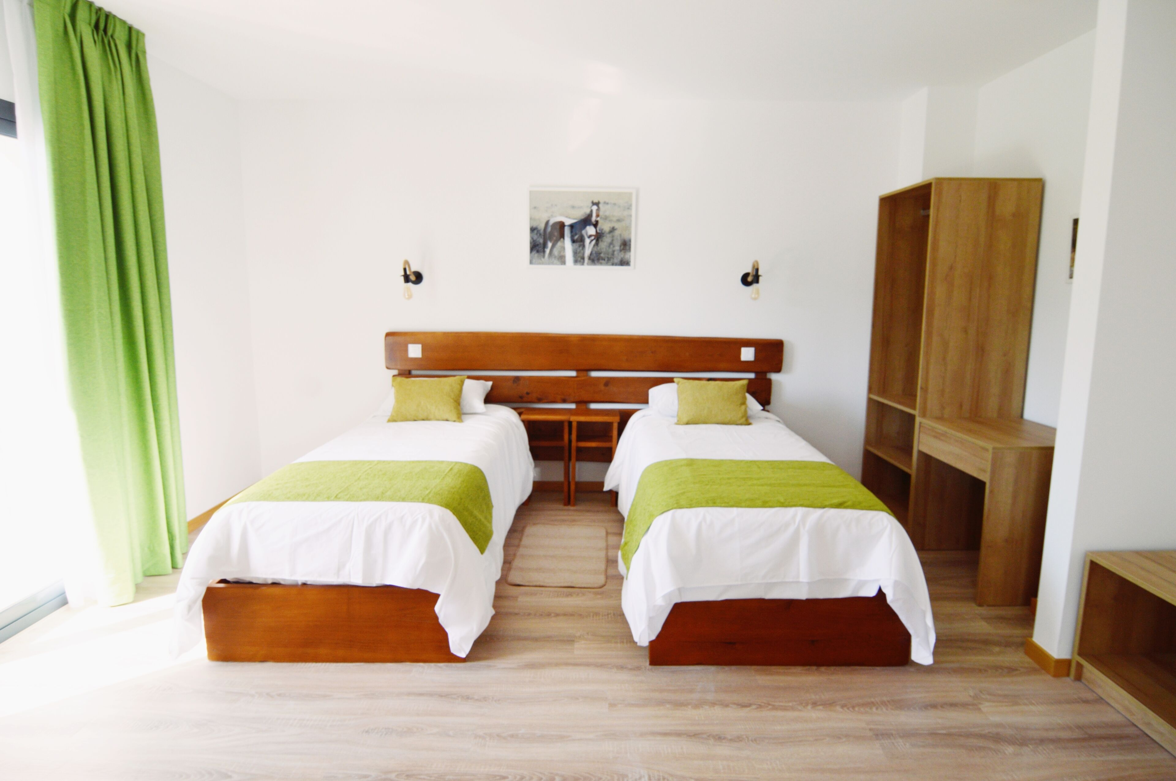 A room with two beds, a wooden headboard, a green curtain, and a wooden wardrobe.