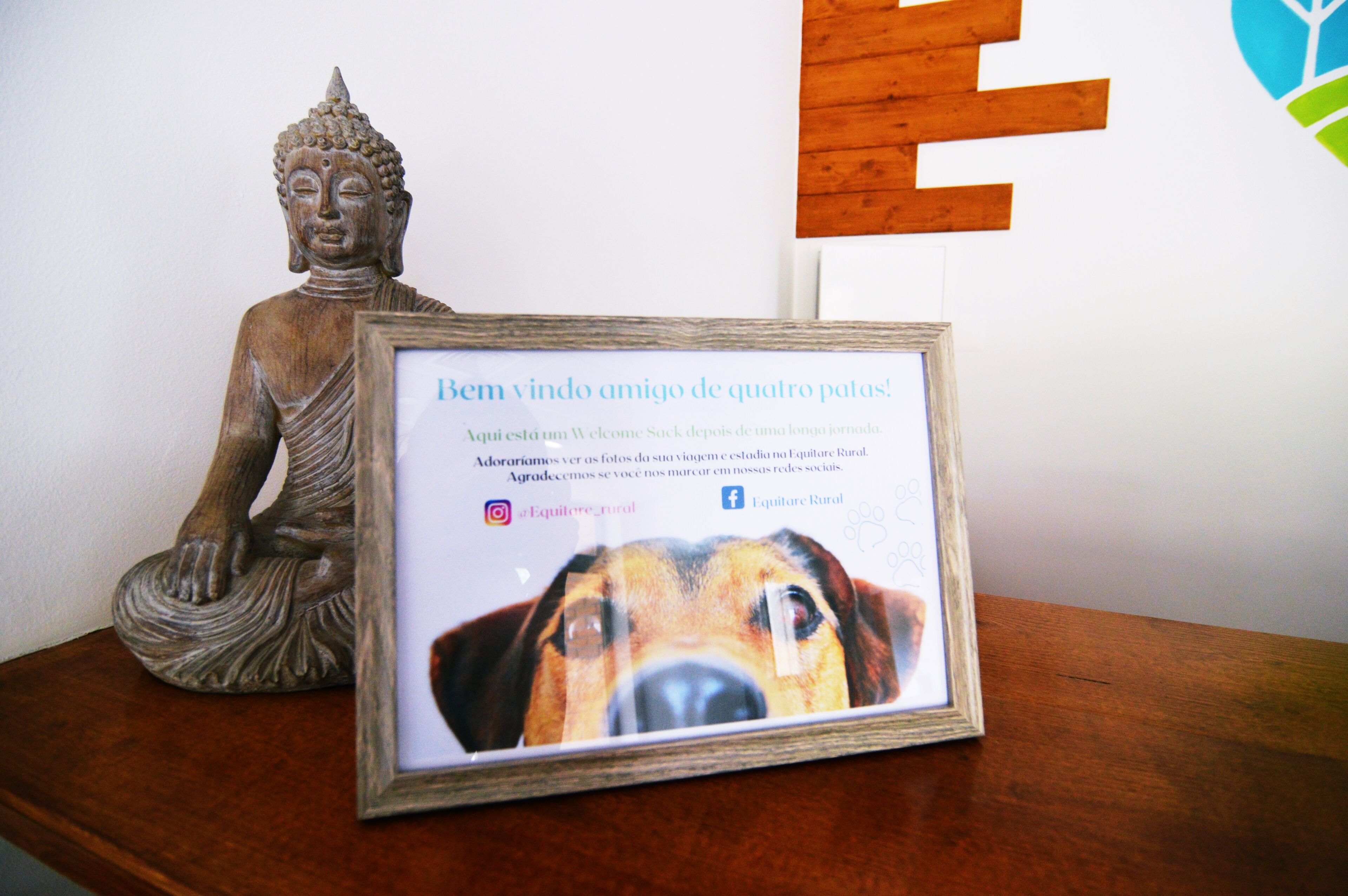 A framed welcome message with a dog's photo, a wooden Buddha statue, and a wooden sign with a tree logo.