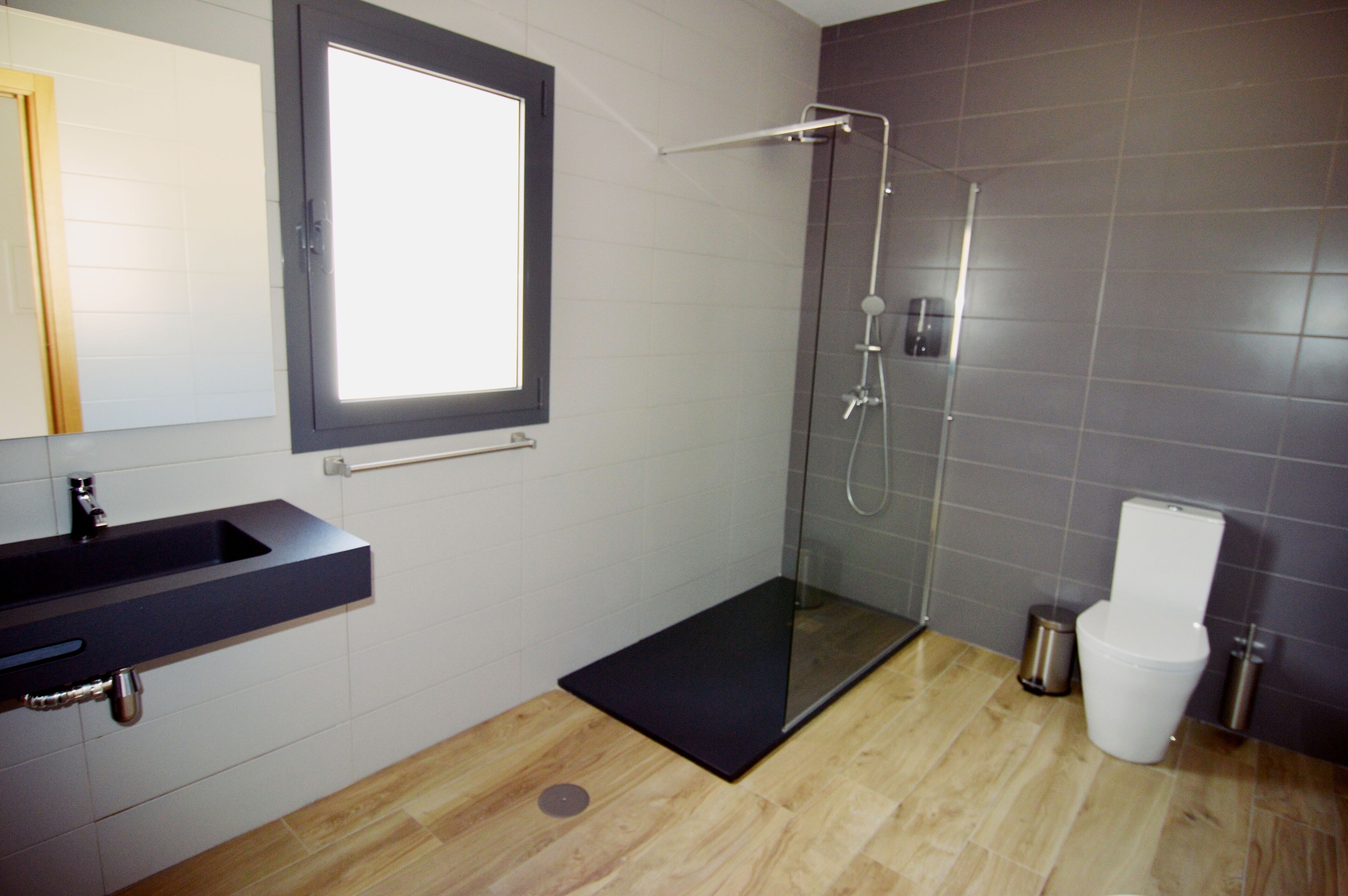 A modern bathroom with a glass-enclosed shower, a black sink, and a toilet.