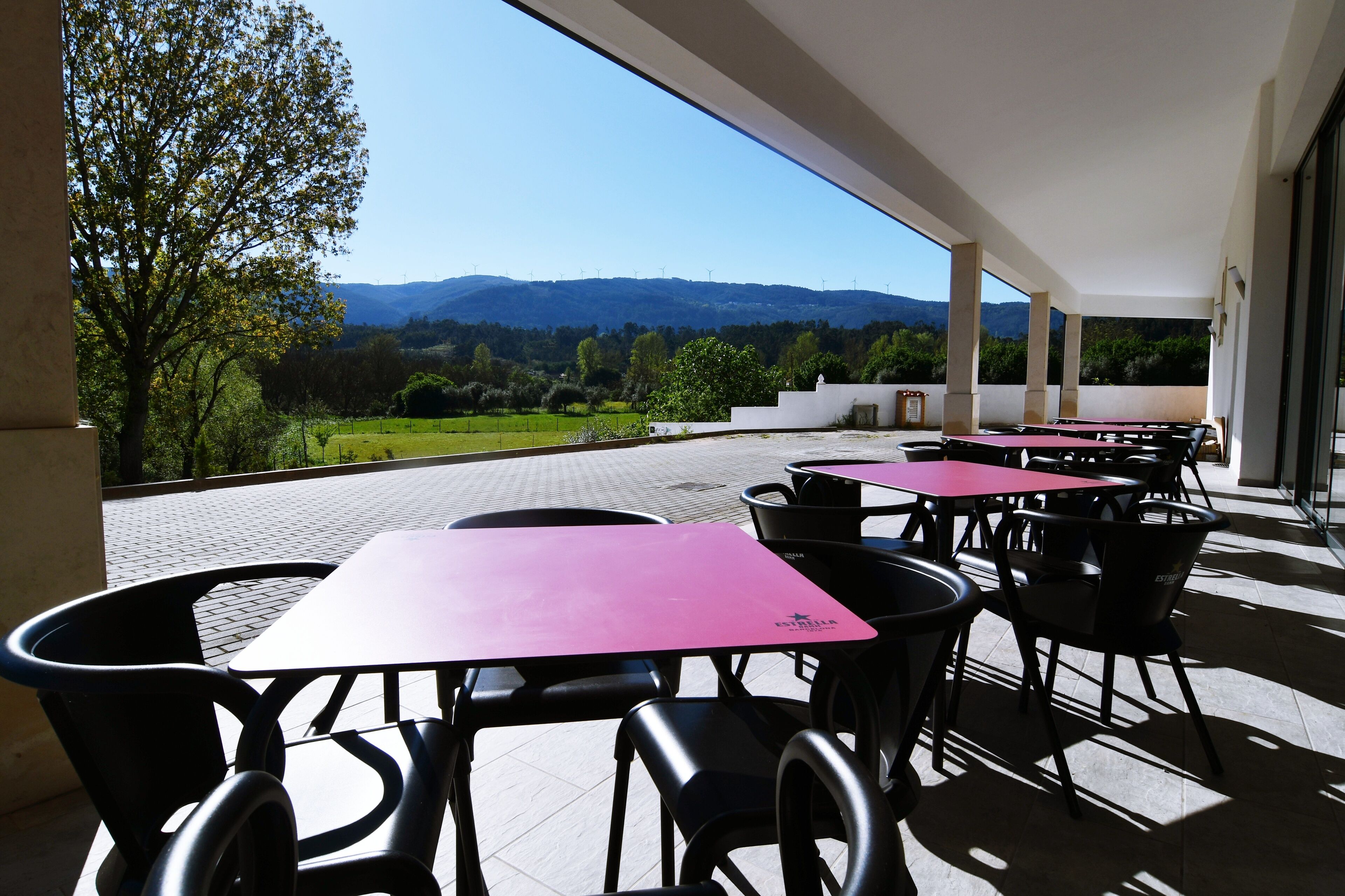Une terrasse avec des tables et des chaises, une vue sur la campagne et un bâtiment au design moderne.
