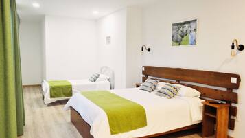 A hotel room with a large bed, a smaller bed, a wooden nightstand, a wall-mounted light fixture, and a picture on the wall.