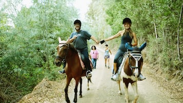 Two people riding horses on a dirt path surrounded by trees.
