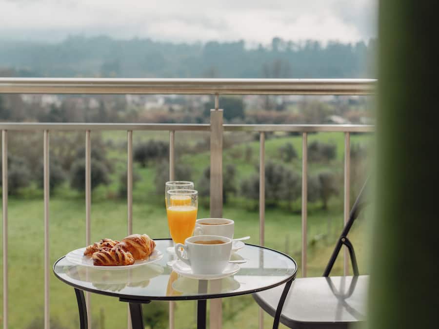 A balcony with a table set for breakfast, including croissants, coffee, and orange juice.