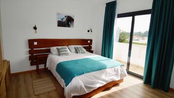 A bedroom with a wooden bed, a view through a large window, and a painting on the wall.