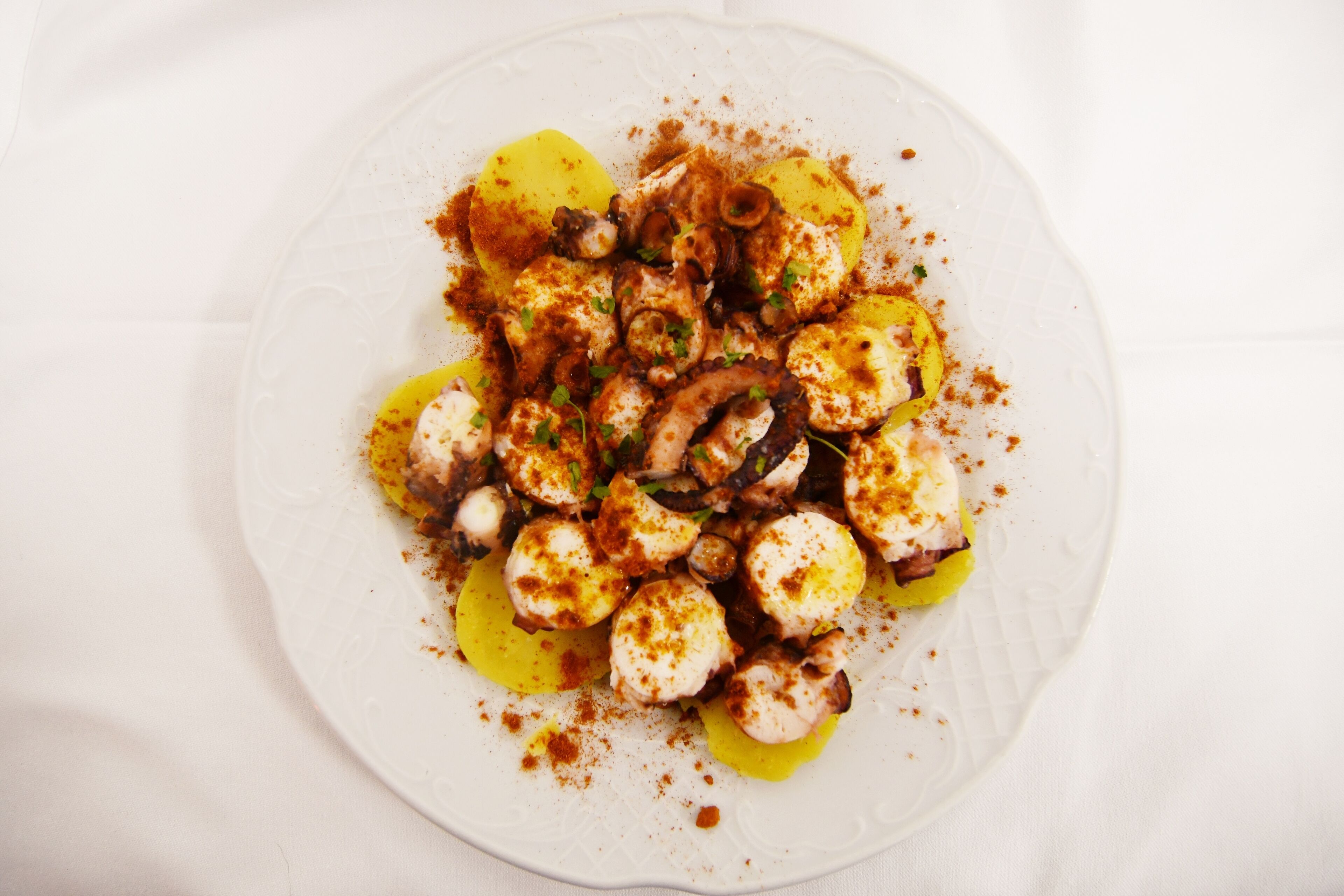 A white plate with a dish of octopus and potatoes, garnished with herbs and spices.