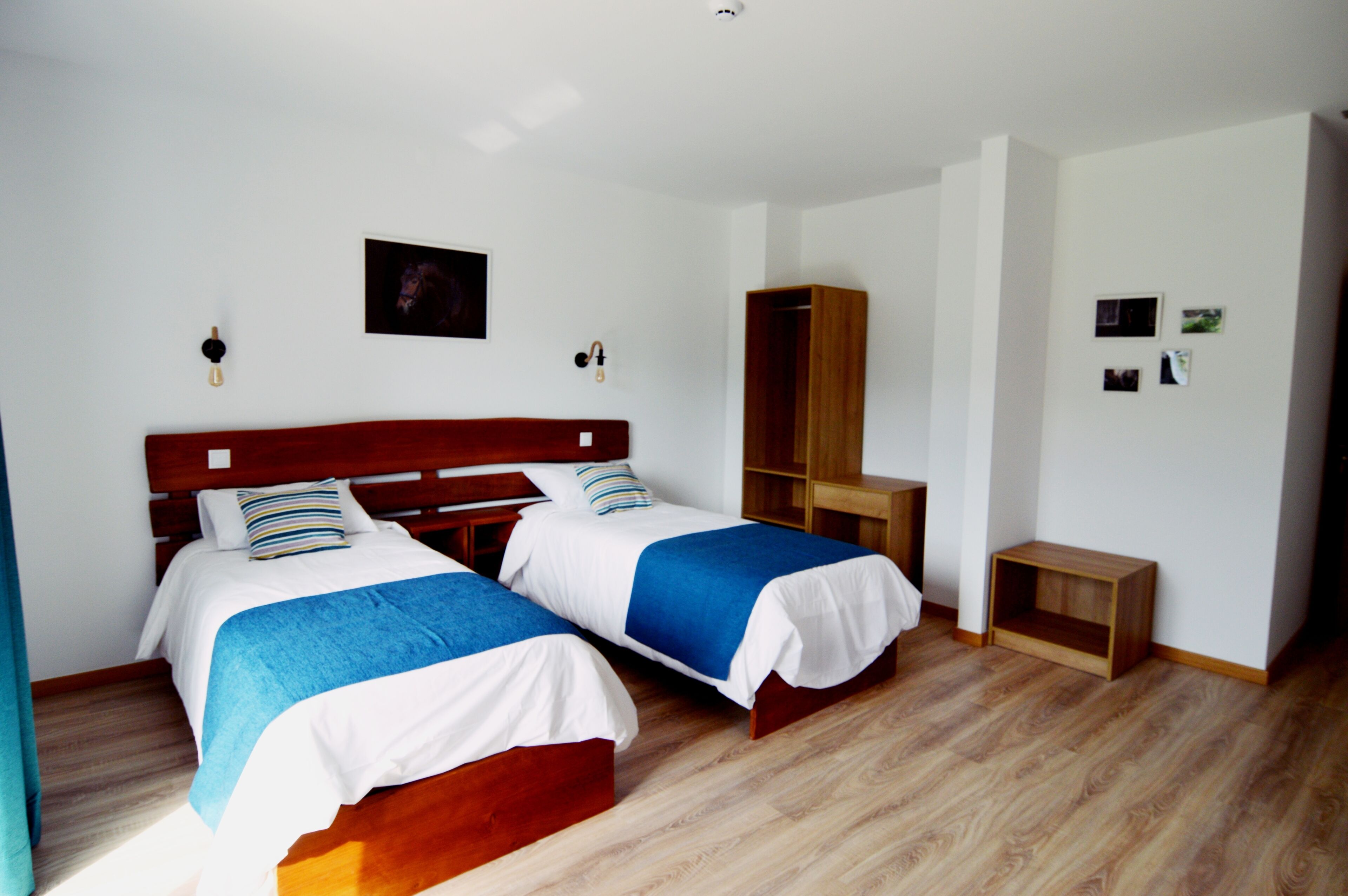 Habitación de hotel con dos camas, un armario de madera, una mesita pequeña de madera y un cuadro colgado en la pared.