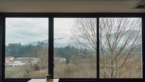 A room with a large window offering a view of a mountainous landscape and a village. - Bed and Breakfast Equitare Rural  (Miranda do Corvo)