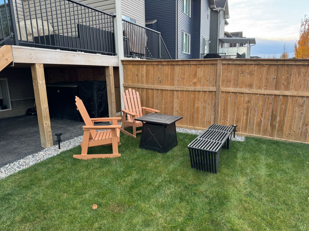 A backyard with a wooden deck, two rocking chairs, a small table, and a black grill.