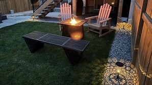 An outdoor patio with a fire pit, two Adirondack chairs, and a bench. - Southern Horizons | Mini Nordic Spa | Fenced Yard (Cochrane)