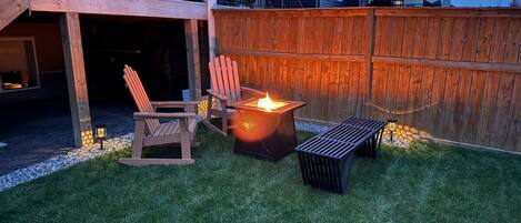 Ein Garten mit Feuerstelle, Holzstuhl und Bank.