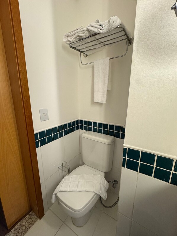Um banheiro pequeno com vaso sanitário, um porta-toalhas com toalhas dobradas e painel de azulejos.