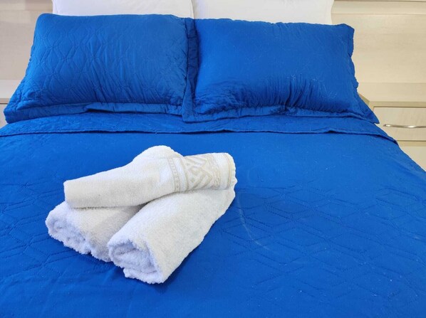 A bed with a blue quilt and two pillows, a white towel, and a wooden headboard. - Apartamento Master em Curitiba (Curitiba)