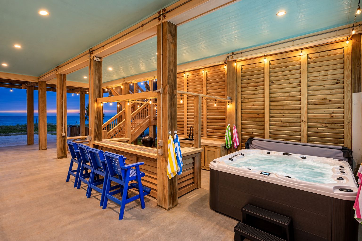Un espacio exterior de madera con jacuzzi, asientos y una escalera que conduce a una terraza superior.