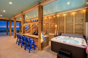A wooden outdoor area with a hot tub, seating, and a staircase leading to an upper deck.