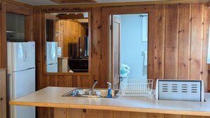 Eine Küche mit Holzwänden, einer zentralen Kochinsel mit Hockern, einem Kühlschrank und einer Mikrowelle.