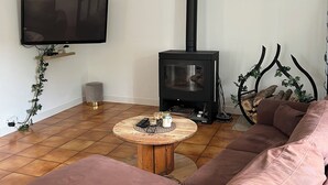 Olohuoneessa on suuri sohva, seinälle asennettu televisio, musta puukamiina ja pyöreä puinen sohvapöytä.