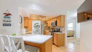 A modern kitchen with wooden cabinets, a central island, and a dining area with white chairs. - Pool - 3 bedrooms - 2 baths - Pet Friendly - 3 Miles to Beach (Bonita Springs)