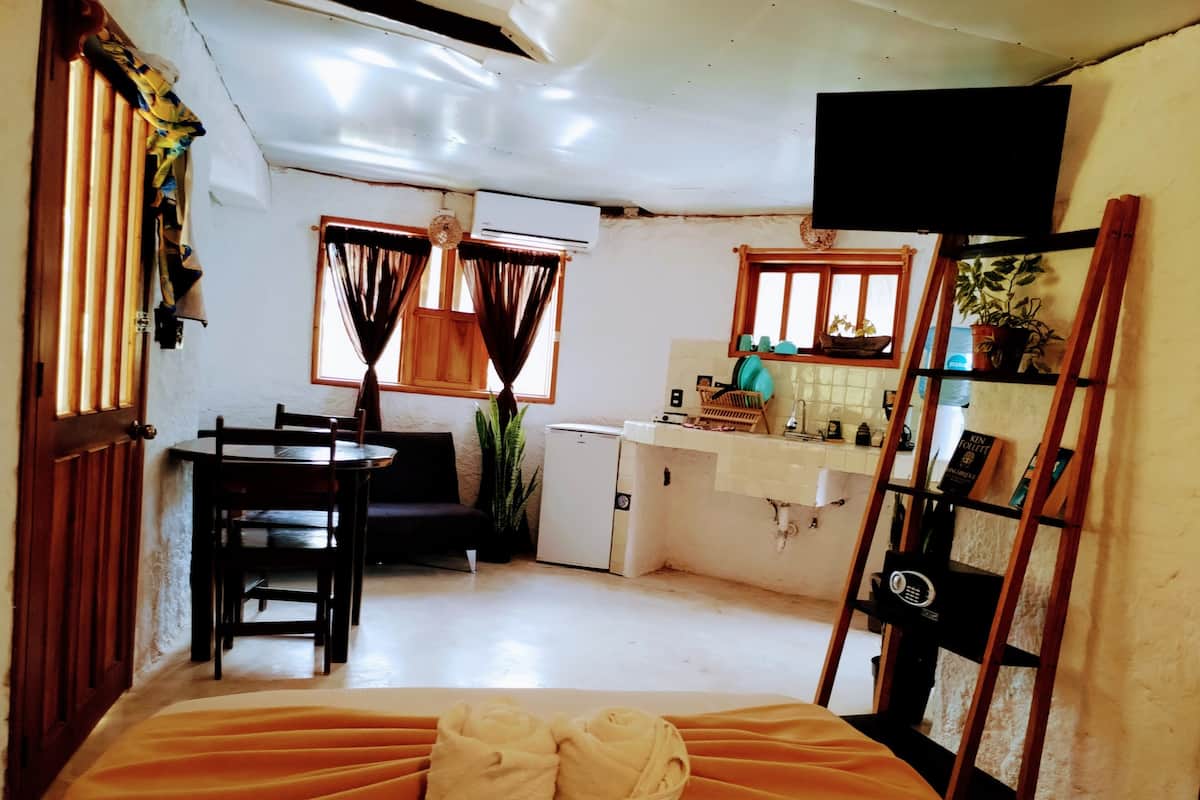 Une chambre de taille réduite comprenant un lit, une petite kitchenette, un coin repas et un téléviseur fixé au mur.
