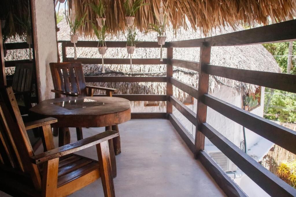 A wooden table and chairs on a balcony with a thatched roof and potted plants.