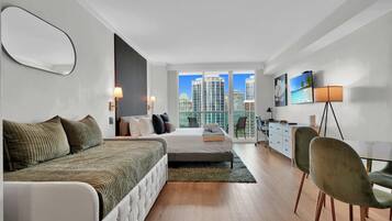Un dormitorio moderno con cama, mesitas de noche, un escritorio y vistas a la ciudad.