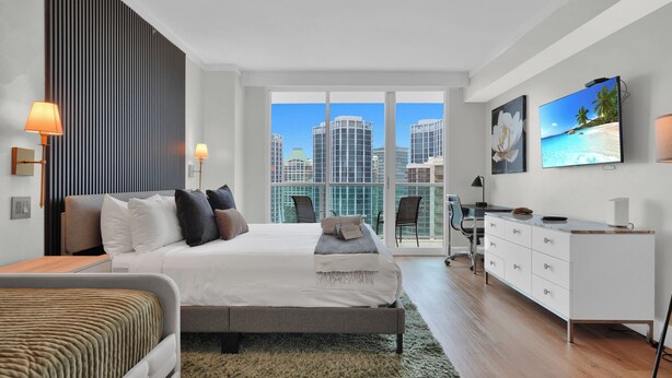 A modern bedroom with a large bed, a desk, and a TV. - Find Tranquility in the Grove (Miami)