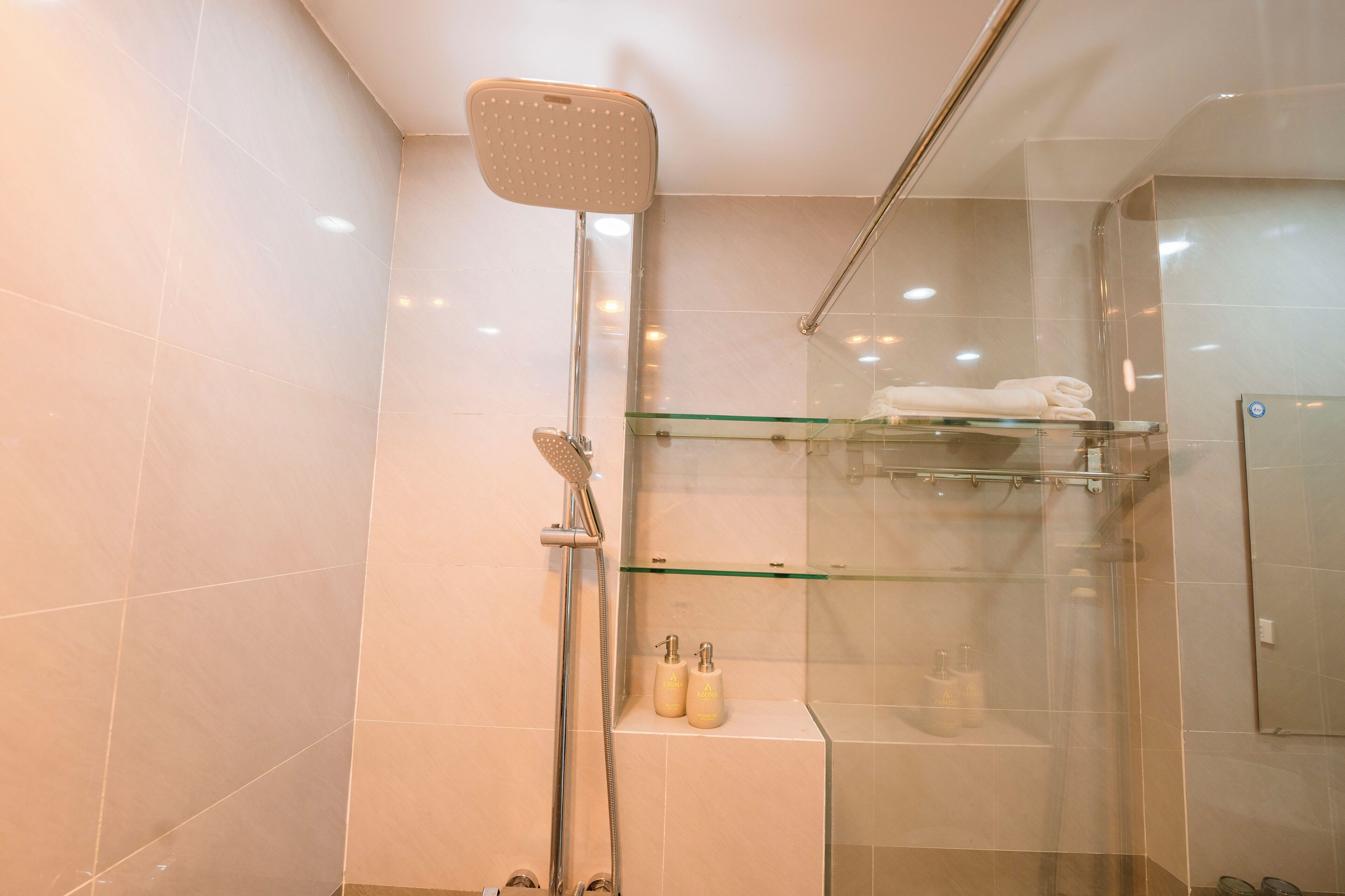 Ducha moderna con cabina de vidrio, repisa de vidrio con artículos de aseo y puerta de vidrio.
