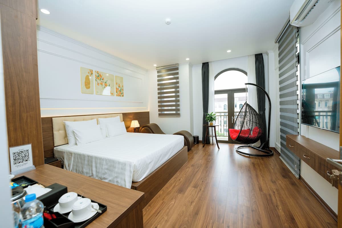 Une chambre d’hôtel moderne avec un grand lit, un bureau agrémenté d’un plateau de produits de courtoisie, un fauteuil suspendu et une vue sur la ville par la fenêtre.